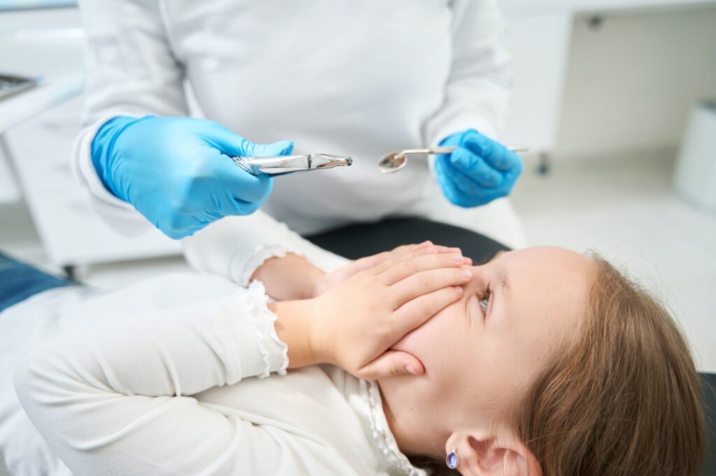 Child feeling scared of pediatric dentist with medical instruments