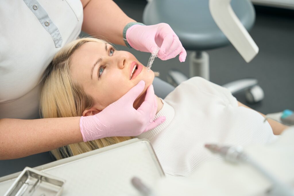 Dentist holding clear aligners near patient's mouth